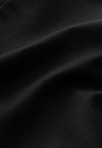 Czarna tkanina o gładkiej, lekko błyszczącej fakturze, z miękkimi, płynącymi fałdami i subtelnymi falami.