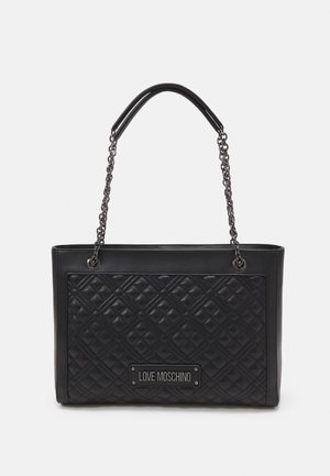 Borsa a tracolla nera trapuntata con manici a catena e placca con il logo "Love Moschino" sul pannello frontale su uno sfondo bianco.