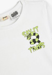 Hvid bomulds t-shirt med et grafisk design, der viser en grøn og sort slange samt teksten "Sig det 3 gange" i lys grøn.
