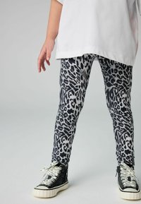 Leggings s uzorkom leoparda u crnoj i sivoj boji s mekom teksturom, upareni s crnim visokom tenisicama s bijelim brandiranim vezicama.