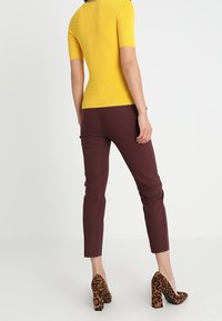 Yellow ribbed short-sleeve top paired with maroon fitted pants and brown leopard print heels, showing a contemporary casual outfit.
