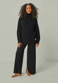 Schwarzer Strick-Turtleneck-Pullover mit lockerer Passform, kombiniert mit schwarzen weit geschnittenen Hosen mit seitlichen Schlitzen. Weiche Textur, minimaler Markenaufdruck.