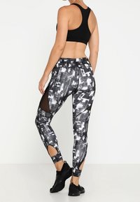 Černý sportovní top doplněný o přiléhavé legíny s monochromatickým geometrickým vzorem, síťovými akcenty a výřezy na lýtkách.
