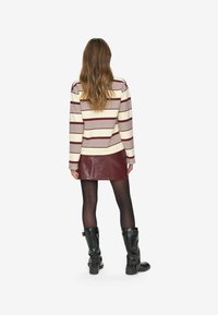 Top a maniche lunghe a righe in crema e bordeaux, abbinato a una minigonna bordeaux lucida, collant neri opachi e stivali neri alti fino al ginocchio.