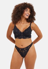 Bralette in pizzo nero e thong coordinato con bordo a scallop, motivo floreale, spalline regolabili e texture trasparente.
