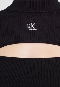 Schwarzes geripptes Oberteil mit einem Stehkragen, Cut-out-Details im Rücken und einem weißen bestickten "ck"-Logo in der Nähe des Kragens.