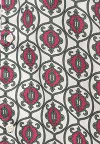 Bawełniana tkanina z białym tłem, na którym powtarza się ozdobny wzór różowych i zielonych kwiatowych kształtów oraz elementów dekoracyjnych, z detalem guzika.