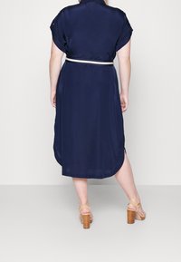 Námořnická midi košilová šaty s krátkým rukávem, páskem v pase, bočními rozparky a hladkou texturou, doplněné hnědými sandály na blokovém podpatku.