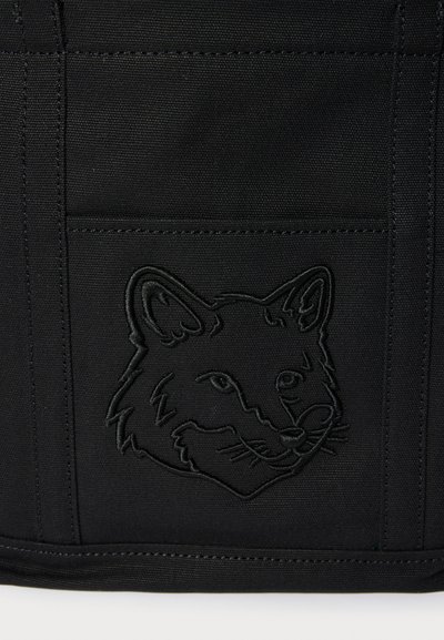 Čierna textília s vyšitým obrysom líšej hlavy na obdĺžnikovom nášivke, zobrazujúcom detailné uši, oči, nos a fúzy.