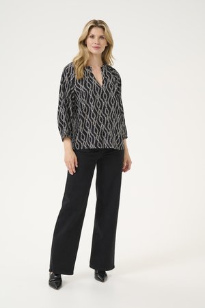 Black patterned blouse with white geometric design, v-neckline, and three-quarter sleeves, paired with black wide-leg jeans and heels.