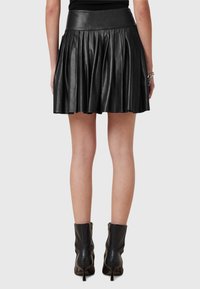 Falda de cuero negra con pliegues y cintura alta, que muestra una textura suave y un diseño ajustado, combinada con botines negros.
