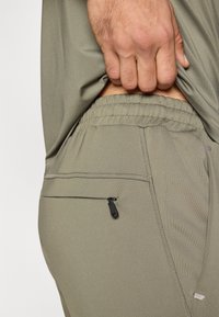 Ελαφριά χακί αθλητικά παντελόνια από λείο ύφασμα. Διαθέτο�υν ελαστική μέση και μικρή τσέπη με φερμουάρ στον γοφό.