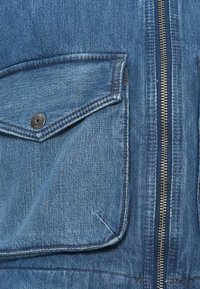 Denimjakke med frontglidelås, brystlomme med trykknapp og teksturert blått stoff.
