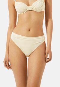 Ensemble de bikini de couleur crème comprenant un haut bandeau avec un détail en nœud et un bas taille haute, fabriqué en tissu lisse avec une texture douce.