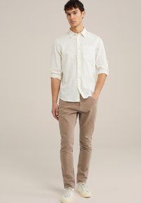 Bela, vzorirana srajca z dolgimi rokavi in  gumbi na ovratniku ter enim žepom na prsih, v kombinaciji s svetlobradimi slim-fit hlačami in belimi supergami.