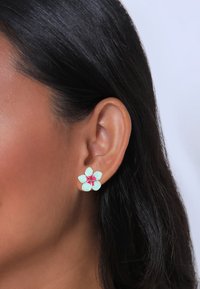 Blütenförmige Ohrringe mit mintgrünen Blütenblättern und einer pinken Mitte, aus einem glänzenden Material, die mit einem Stecker am Ohr befestigt werden.