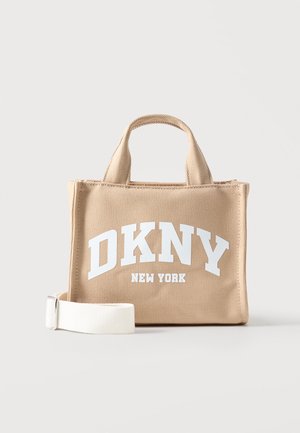 Béžová plátenná taška s krátkymi rúčkami, bielym nastaviteľným ramenným popruhom a nápisom "DKNY New York" veľkými bielymi písmenami.