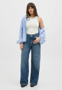 Hvid tanktop med sort kant, parret med en lys blå stribet oversized skjorte. Blå vidde jeans med høj talje. Sorte hælesko.