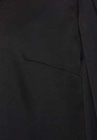 Tissu noir avec une texture lisse, comportant un détail de poche cousue. Le design inclut des lignes épurées et une forme structurée.