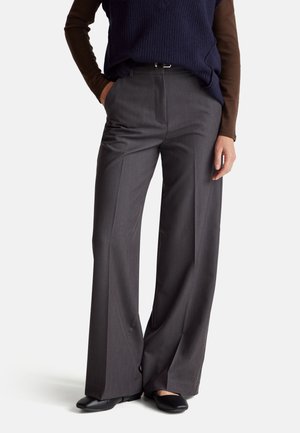 Pantalons à jambes larges en tissu gris, présentant un design ajusté, des plis avant et une taille mi-haute. Des chaussures plates noires complètent le look.