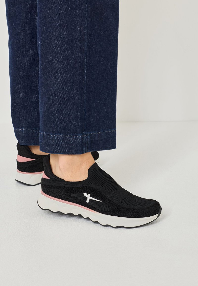 Svarta stickade sportskor med en texturerad ovandel och vit logotyp, med en tjock vit och rosa sula, bärs med mörka denimbyxor.