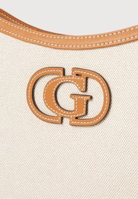Beige canvas tas met een bruine leren accent en een in elkaar grijpend "C"- en "G"-logo, omlijnd met contrasterende witte stiksels.