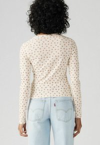 Langärmliges Oberteil in Creme mit gerippter Struktur, das mit einem verstreuten Blumenmuster in Rost versehen ist. Gepresstes Design mit leichtem Rundhalsausschnitt hinten.