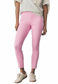 Roze skinny jeans met een gladde textuur en een aansluitend ontwerp, voorzien van een middelhoge taille en een subtiele glans. Gecombineerd met witte sneakers.