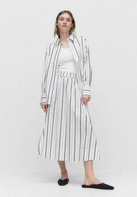 Hvidstribet bluse og matchende nederdel med elastrisk talje; model i sorte flade slippers, enkelt hvid tanktop under.