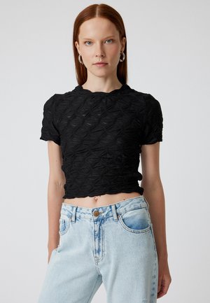 Haut noir court en tissu texturé et à motifs avec un col rond, associé à un jean en denim léger et déchiré bleu.