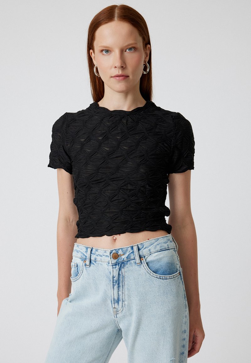 Sort cropped top med struktureret, mønstret stof og rund halsudskæring, parret med lyseblå, slidte denimjeans.
