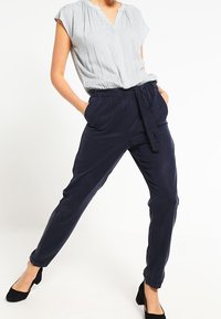 Námořnické kalhoty s tkaničkovým pasem a bočními kapsami, spárované se světle šedou blůzou s puntíky, krátkým rukávem a výstřihem ve tvaru V.