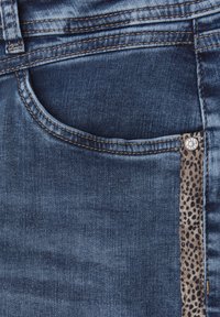 Vaqueros de mezclilla azul oscuro con un bolsillo frontal y un acento de estampado de leopardo a lo largo del costado, con detalles de costura visibles y un botón plateado.
