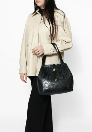 Borsa in ecopelle serpentina nera con due tracolle, forma arrotondata e dettagli in metallo color oro. Indossata insieme a una camicia beige.