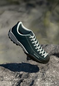Shoe de caminhadas verde em camurça com atacadores brancos, colarinho almofadado, biqueira de borracha e sola texturizada para aderência. Com a marca "SCARPA."