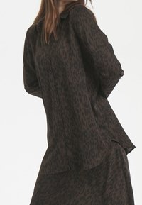 Brun leopardmönstrad knäppskjorta med avslappnad passform och långa ärmar, med en lätt rundad fåll och mjukt, texturerat tyg.