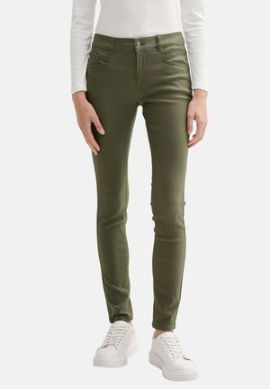 Dunne groene broek van rekbaar materiaal met voorkruiden. Gecombineerd met witte sneakers, die een soepele, aansluitende uitstraling benadrukken.