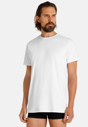 White cotton t-shirt with a crew neckline and short sleeves, displayed on a person wearing black boxer shorts. Simple design, smooth texture.