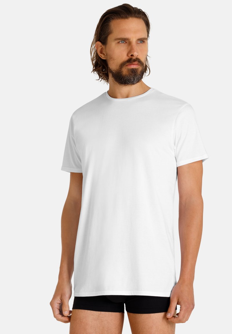 T-shirt bianca in cotone con scollo rotondo e maniche corte, indossata da una persona che porta pantaloni boxer neri. Design semplice, texture liscia.