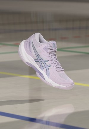 Φωτεινό μωβ αθλητικό παπούτσι Asics με τιρκουάζ λογότυπο που αιωρείται πάνω από το παρκέ ενός εσωτερικού γηπέδου με έγχρωμες γραμμές.