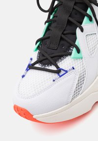 White sneaker with mesh upper, black and turquoise accents, textured leather overlays, and a rubber sole featuring an orange accent.