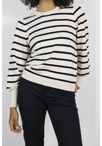 Lichtbeige sweater met zwarte horizontale strepen, ronde halslijn en pofmouwen, gecombineerd met zwarte broek. Geweven materiaal met textuur.