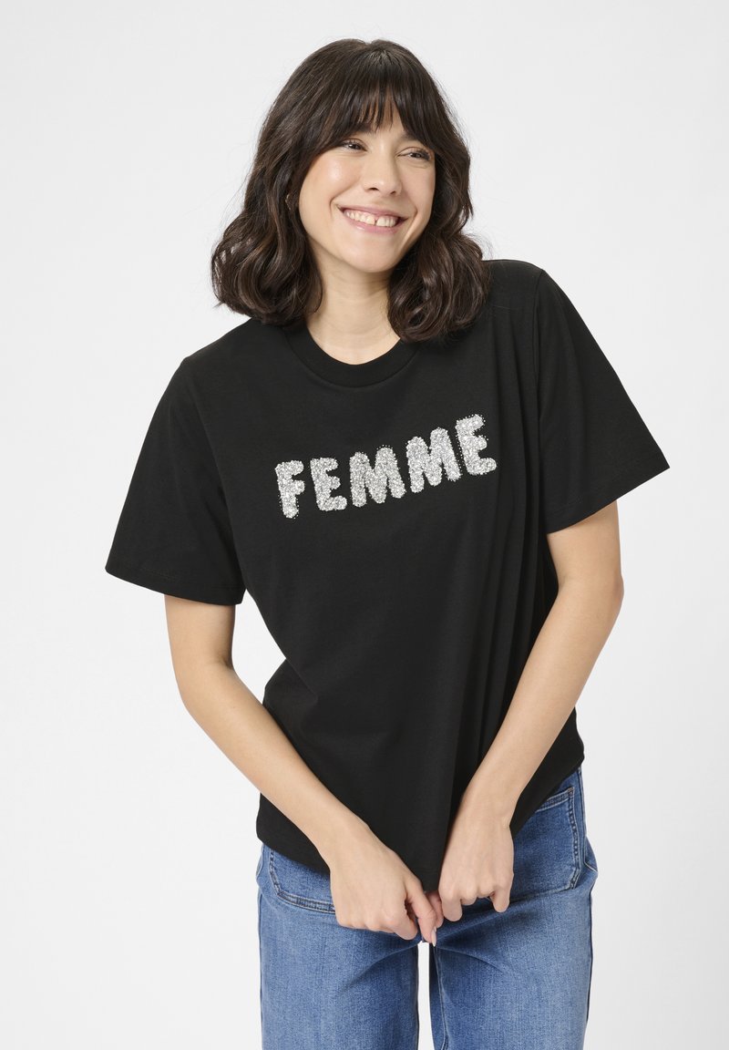 Tricou din bumbac negru, având cuvântul "FEMME" scris cu litere argintii texturate. Croială lejeră cu mâneci scurte. Asortat cu blugi blue.