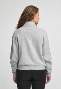 Grå sweatshirt med hög krage, avslappnad passform, ribbade ärmslut och midja. Mjuk textur utan synliga mönster eller detaljer.