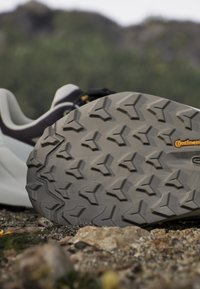 Semelle d'une chaussure de trail avec un motif de bande de roulement profond reposant sur un sol rocheux en extérieur, montrant la marque "Continental" sur la semelle.