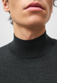 Maglione a collo alto grigio scuro con texture a costine. Vista ravvicinata del colletto e del collo, che evidenzia il tessuto morbido e il design strutturato.