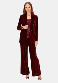 Bordowy welwetowy garnitur z dopasowaną marynarką i spodniami o szerokich nogawkach. Pod spodem top z cekinami, okrągły dekolt, eleganckie dodatki i buty na obcasie z odkrytymi palcami.