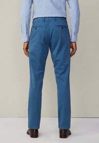 Jasnoniebieskie bawełniane spodnie o prostych nogawkach, z dwiema tylnymi kieszeniami i wyraźnymi szwami; noszone z jasnoniebieską koszulą z długim rękawem.