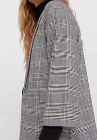 Grijze geruite blazer met een losse pasvorm, voorzien van zwarte en okerkleurige strepen, zachte textuur en brede mouwen. Accentueert met een eenvoudig ontwerp.