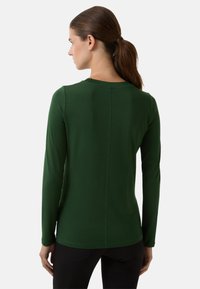 Chemise à manches longues en tissu extensible, de couleur verte, avec un col rond et une silhouette ajustée, dotée de détails de couture au dos.